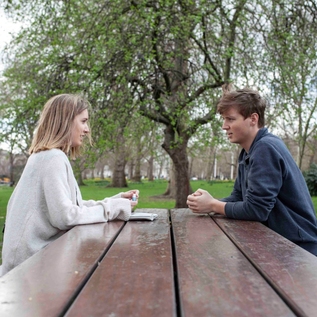 Two people sat in a park with Scentered Aromatherapy Balm with a silver pouch