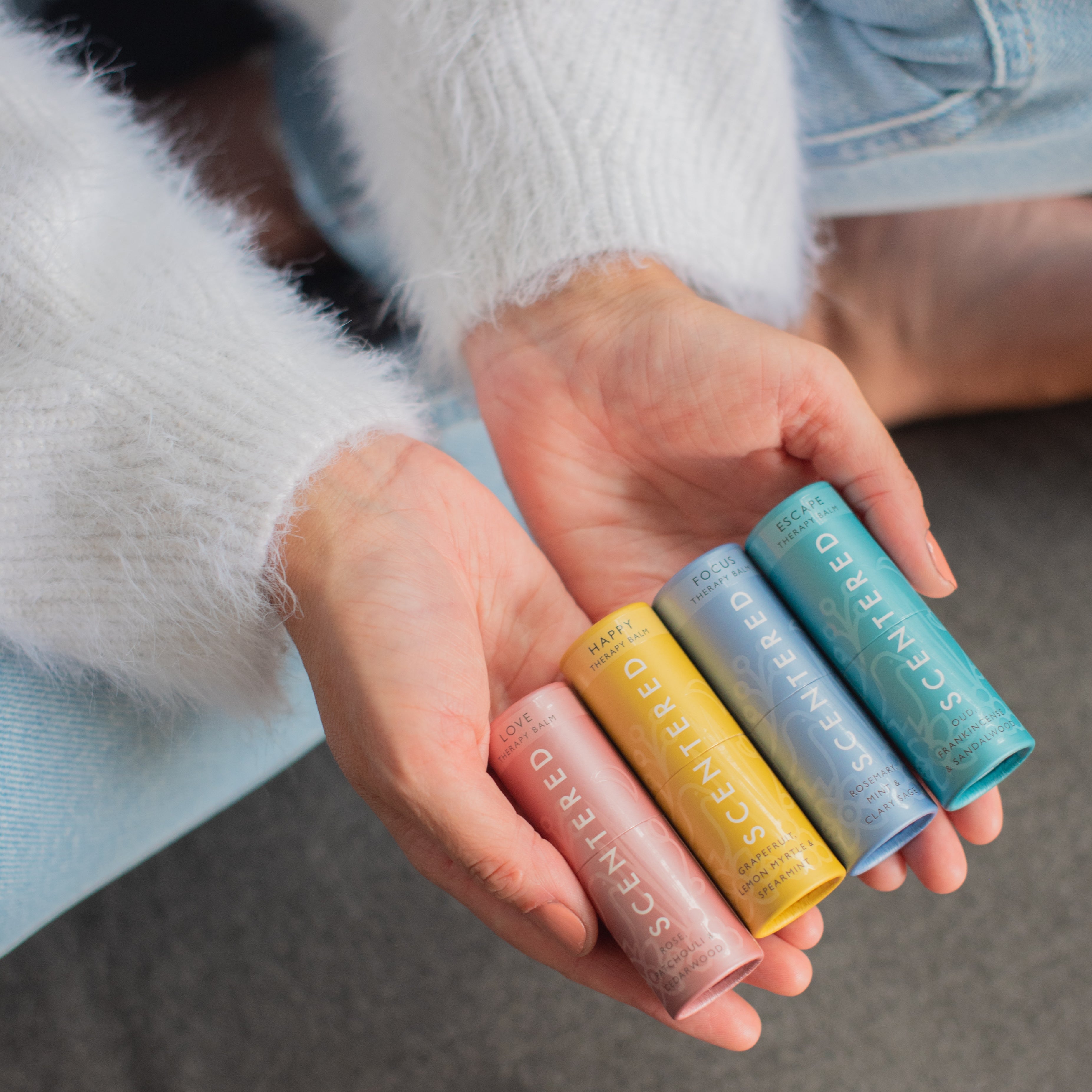 Person holding four balms of different colors in their hands.