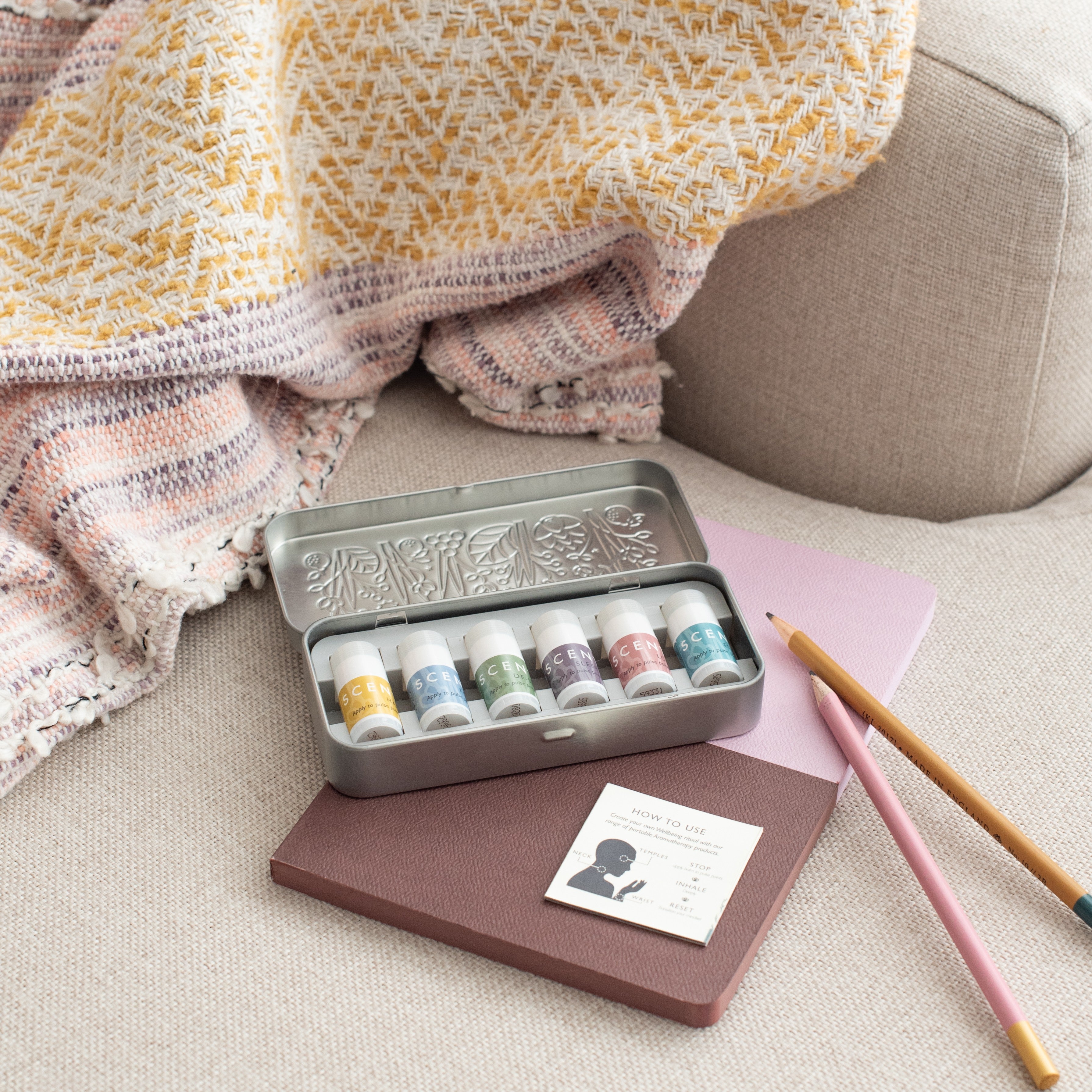 A discovery tin, a pink notebook, and a set of pencils lie on the sofa.