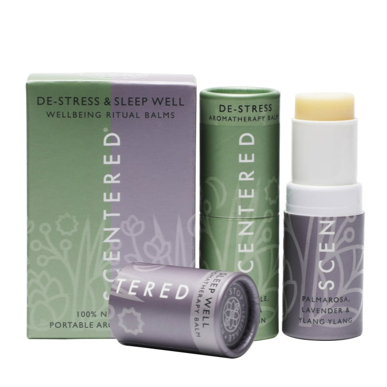 This photo features Scentered's De-Stress & Sleep Well Wellbeing Ritual Balms. There's a box and two portable balm sticks. The green stick is for de-stress balm, and the purple ones are for sleep-well balm.