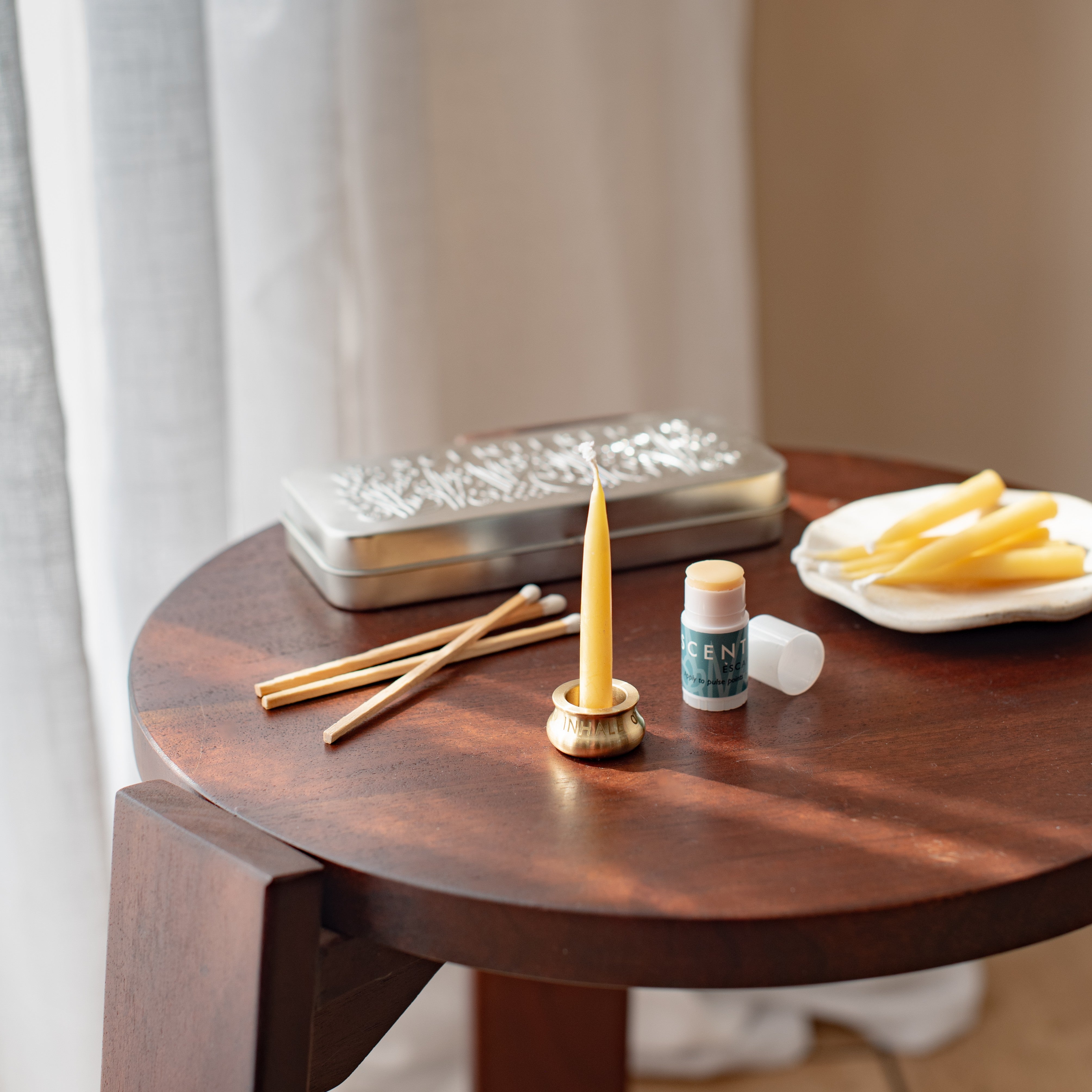 A few candles, an Escape mini balm, and a tin are laid out on the table.