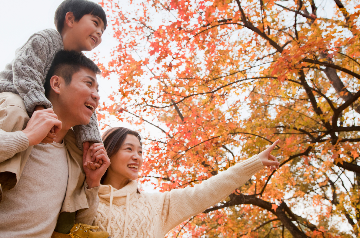 Family of three smiling under autumn tree