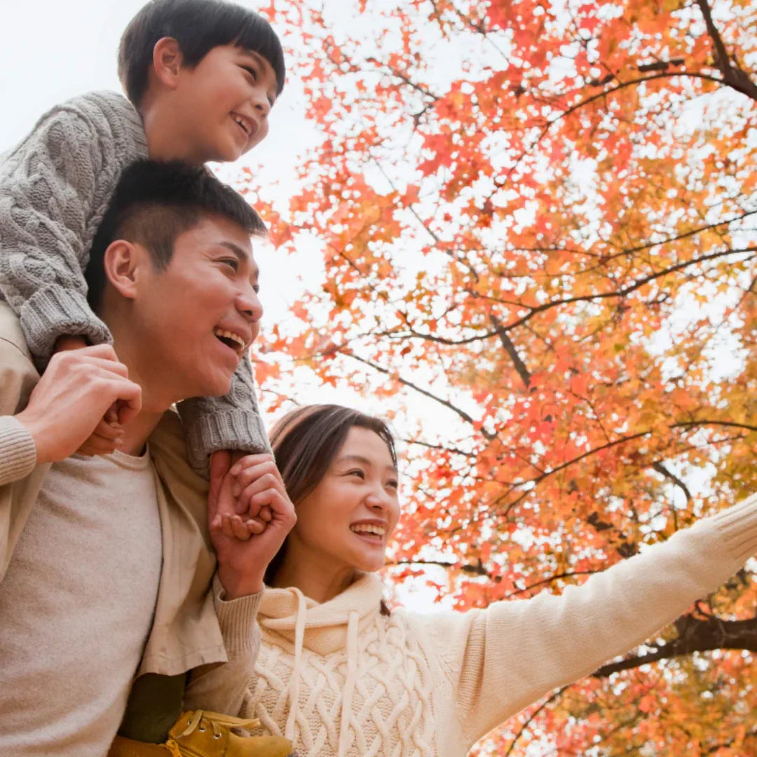 Family of three smiling under autumn tree