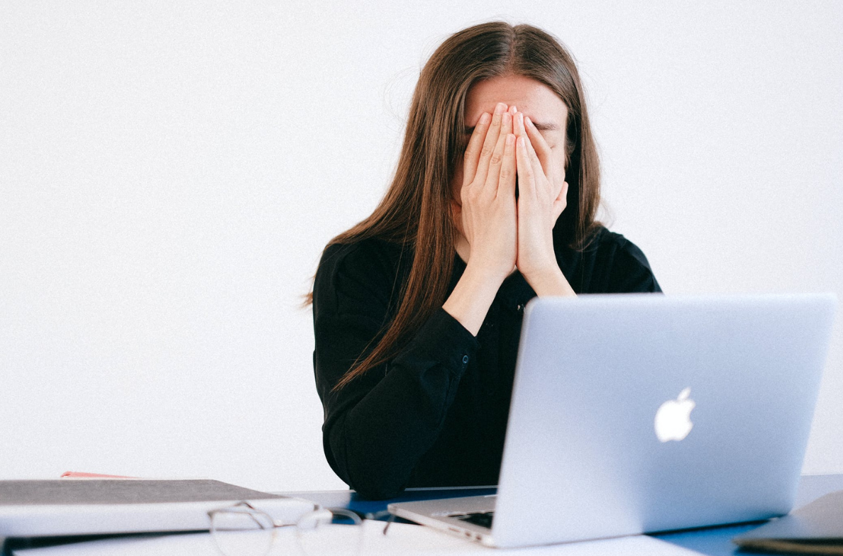 woman covering her face in front of the laptop