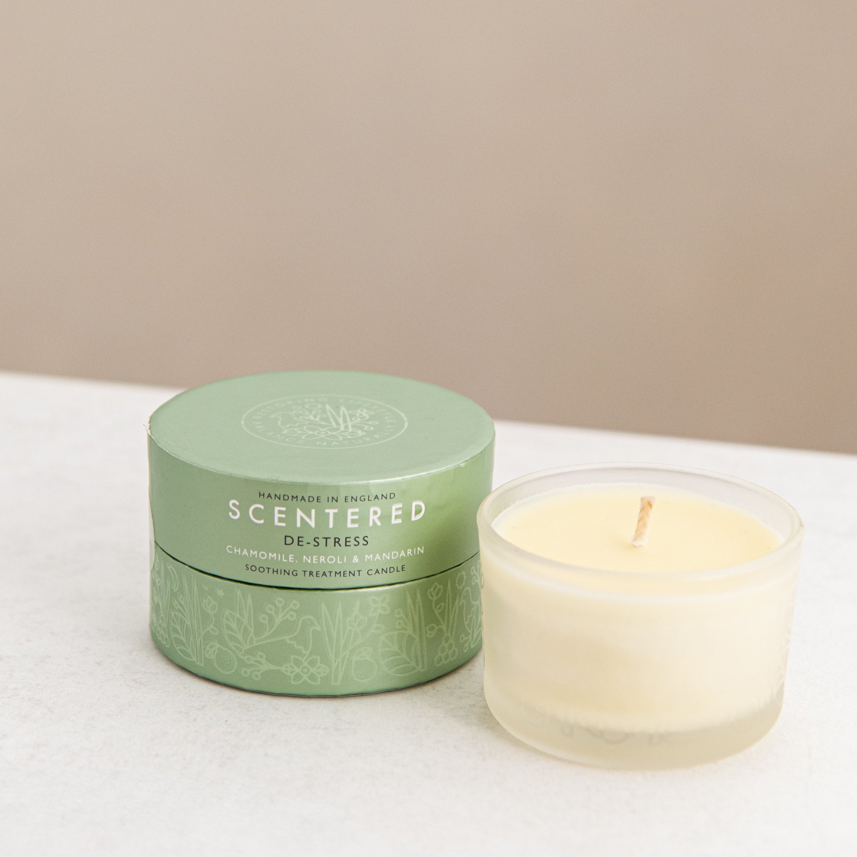 Scented candle and green gift box on a white surface.