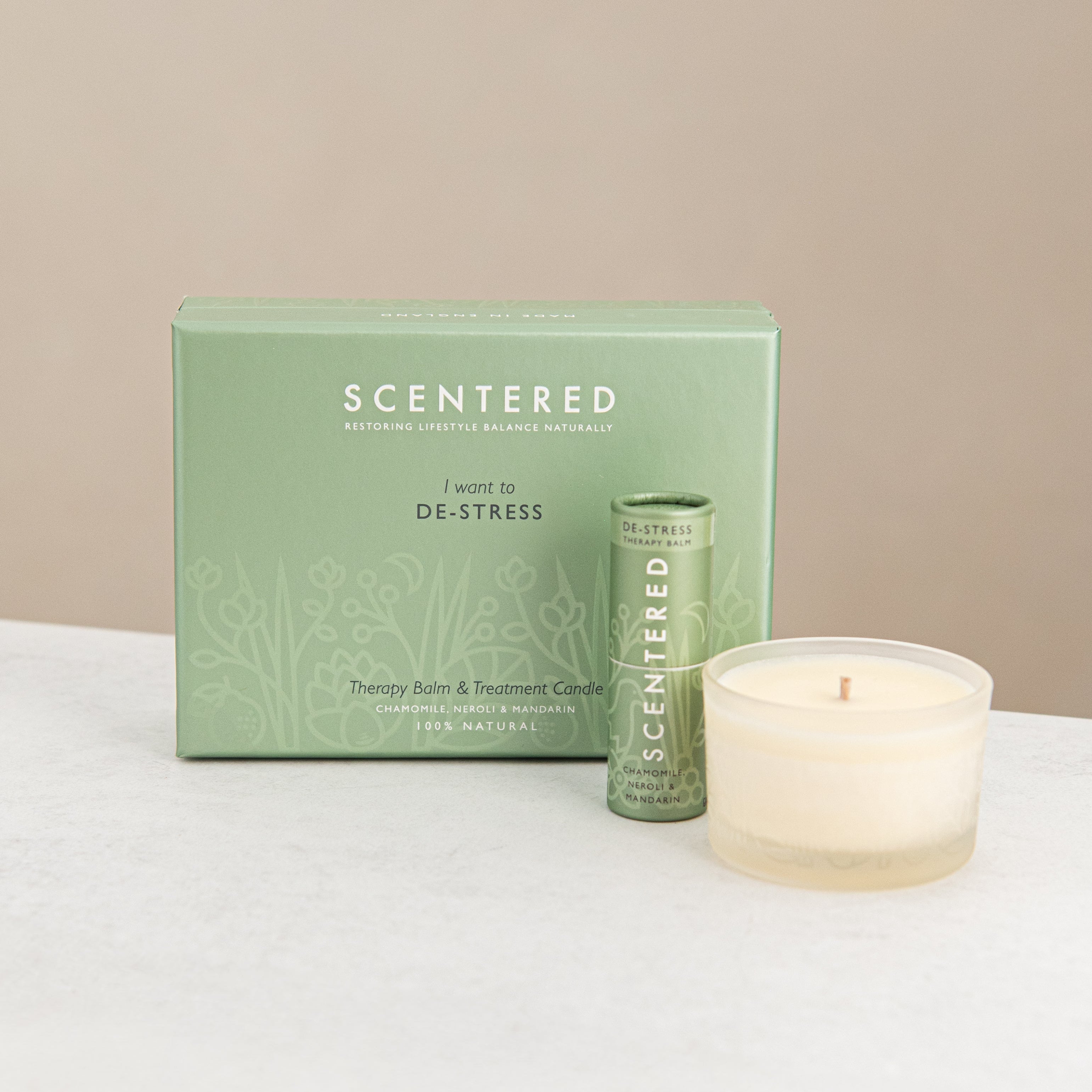 Scentered product packaging with a de-stress balm and candle on a white surface.