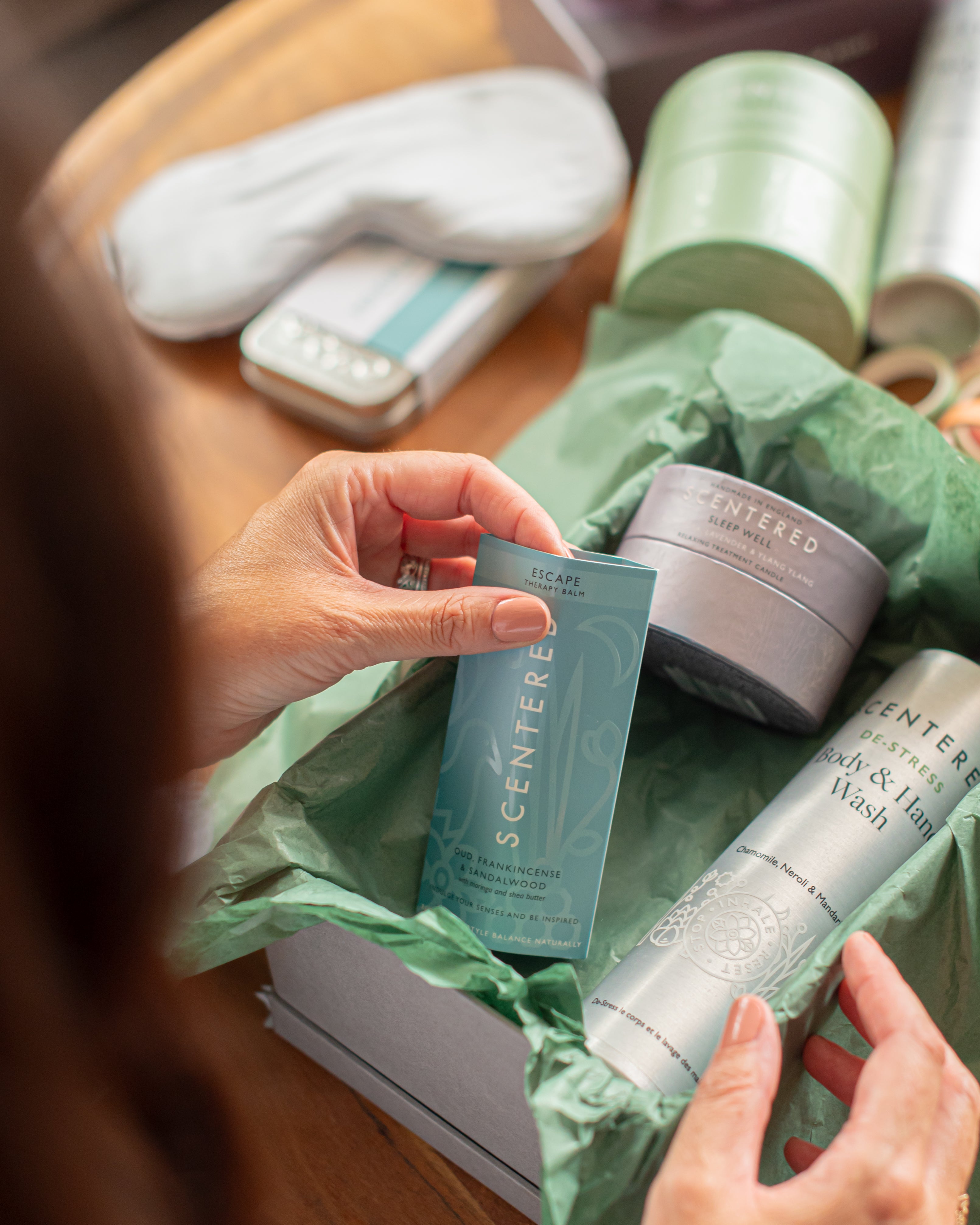 A Woman Touches the escape balm from a gift box complete with sleep well candle and handwash.