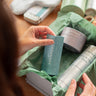 A Woman Touches the escape balm from a gift box complete with sleep well candle and handwash.