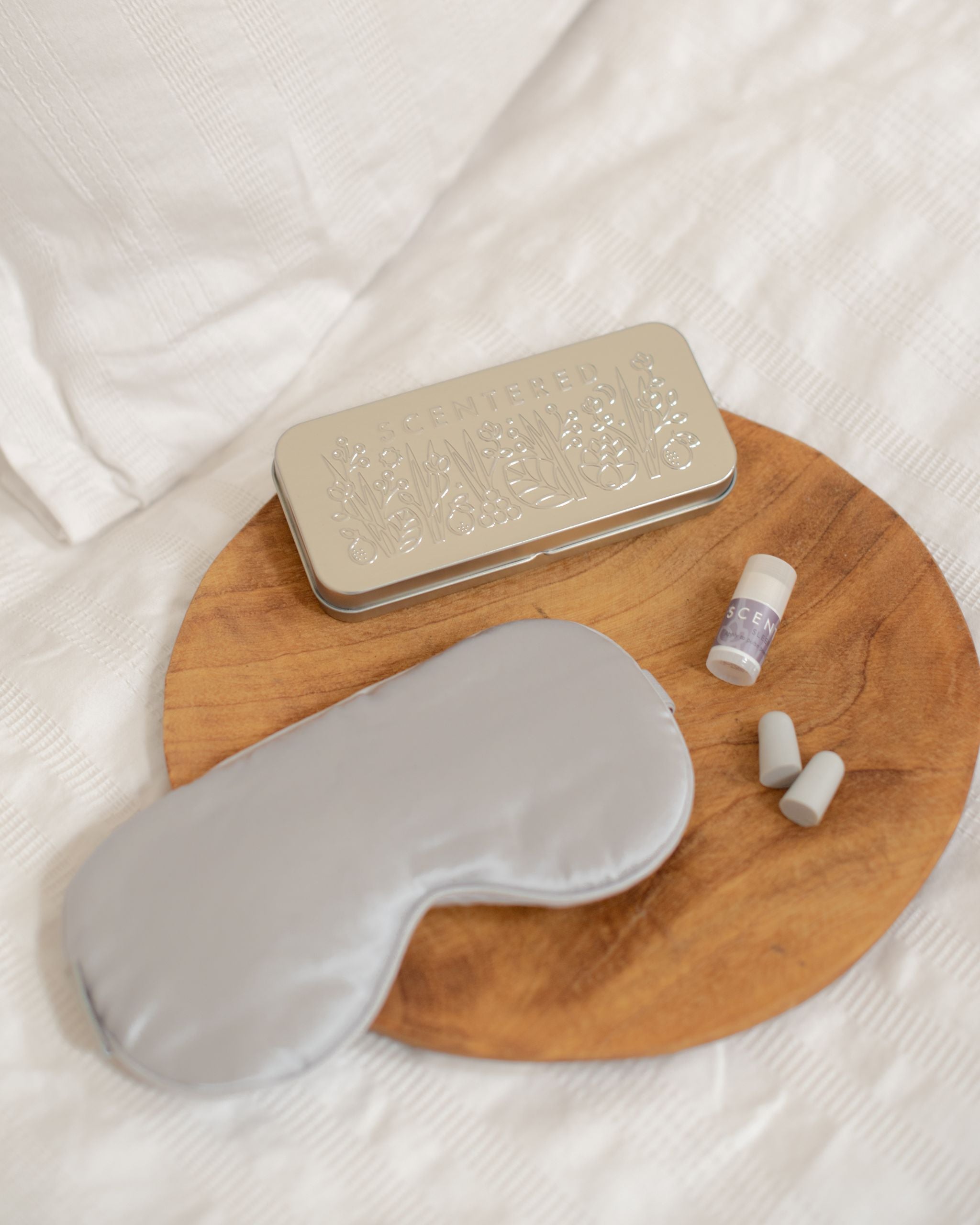 Goodnight Gift Set with Silk eye mask, Sleep Well Mini balm and ear plugs laid out on on bed next to travel tin