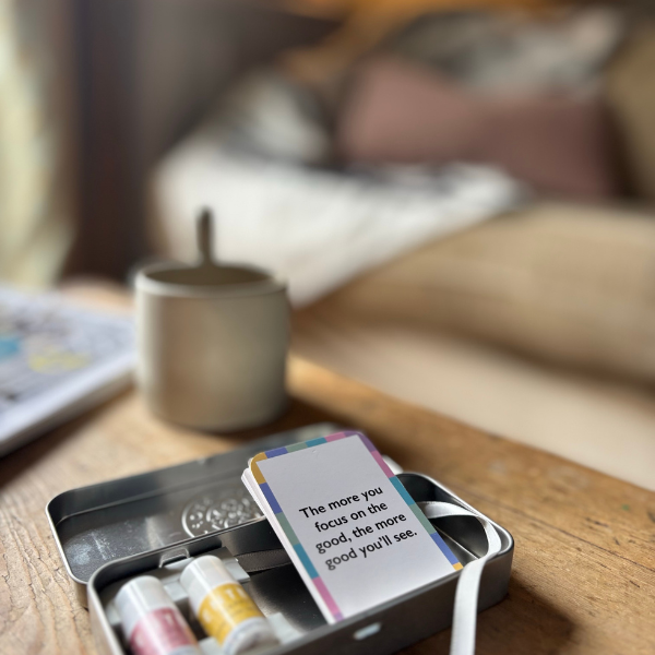 Card with motivational quote and balms in a tin and a mug on the table.