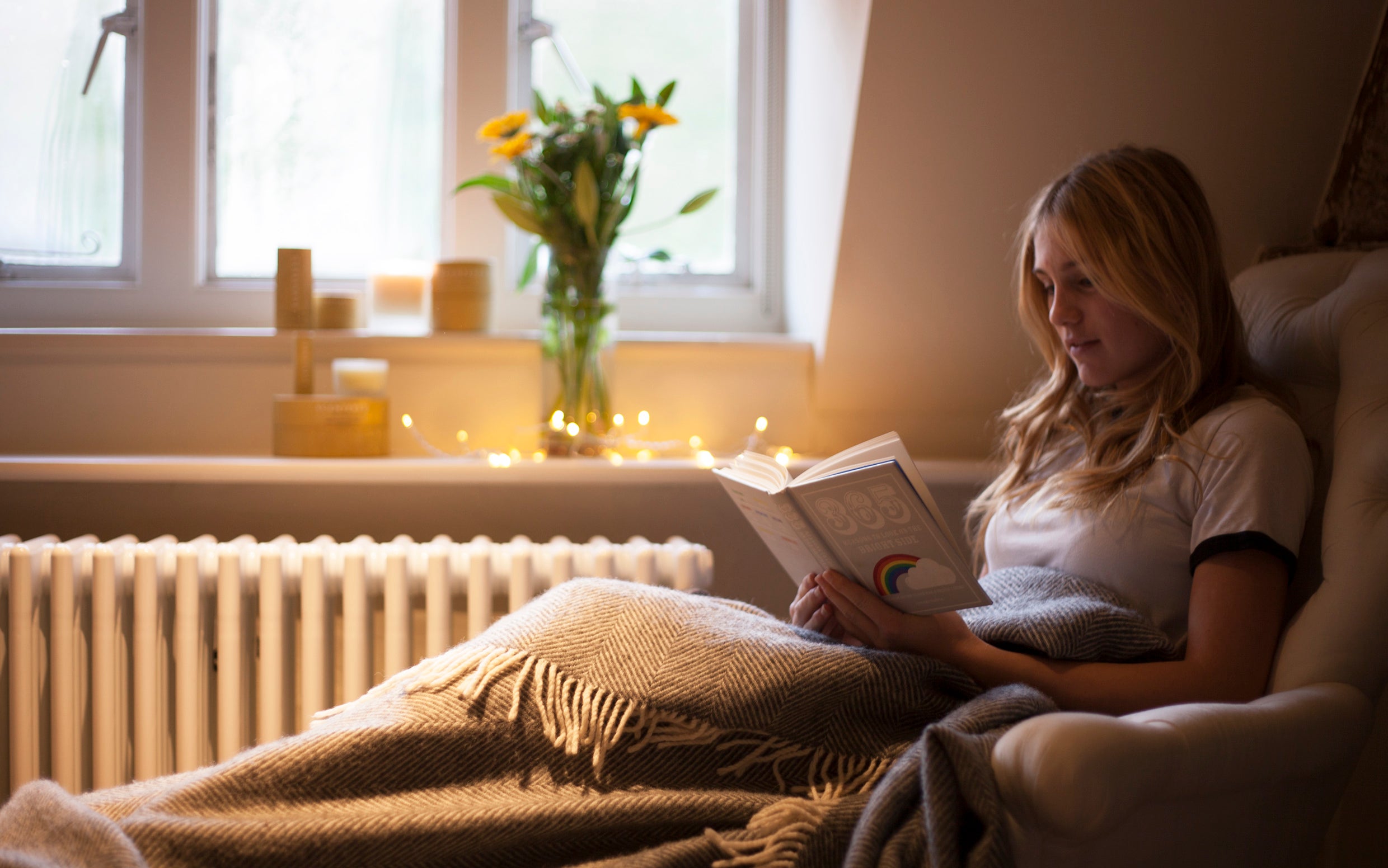 Woman reading a book in a cozy room with soft lighting and decorative elements.