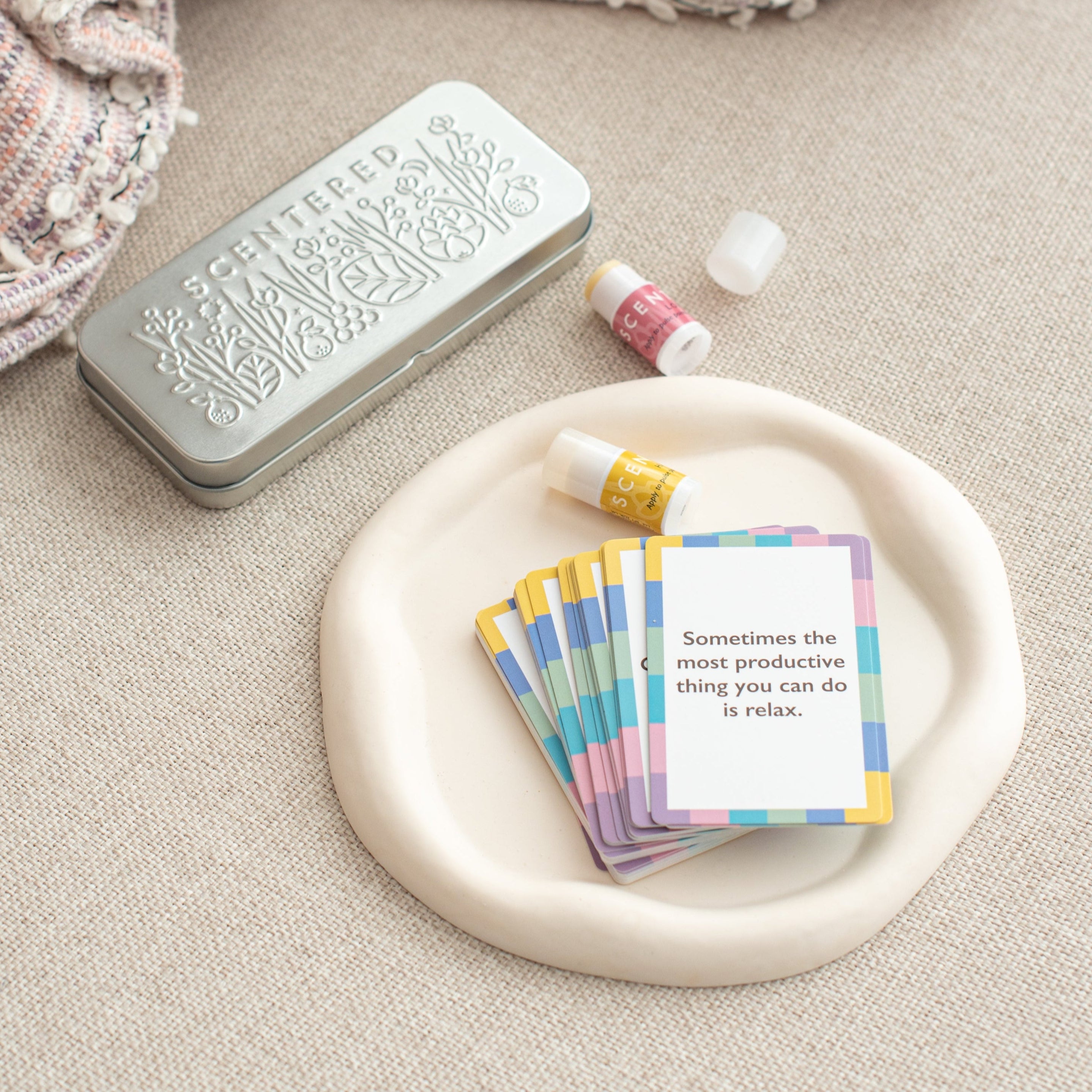 A tin box, a pack of cards, and two mini balms are resting on the sofa.