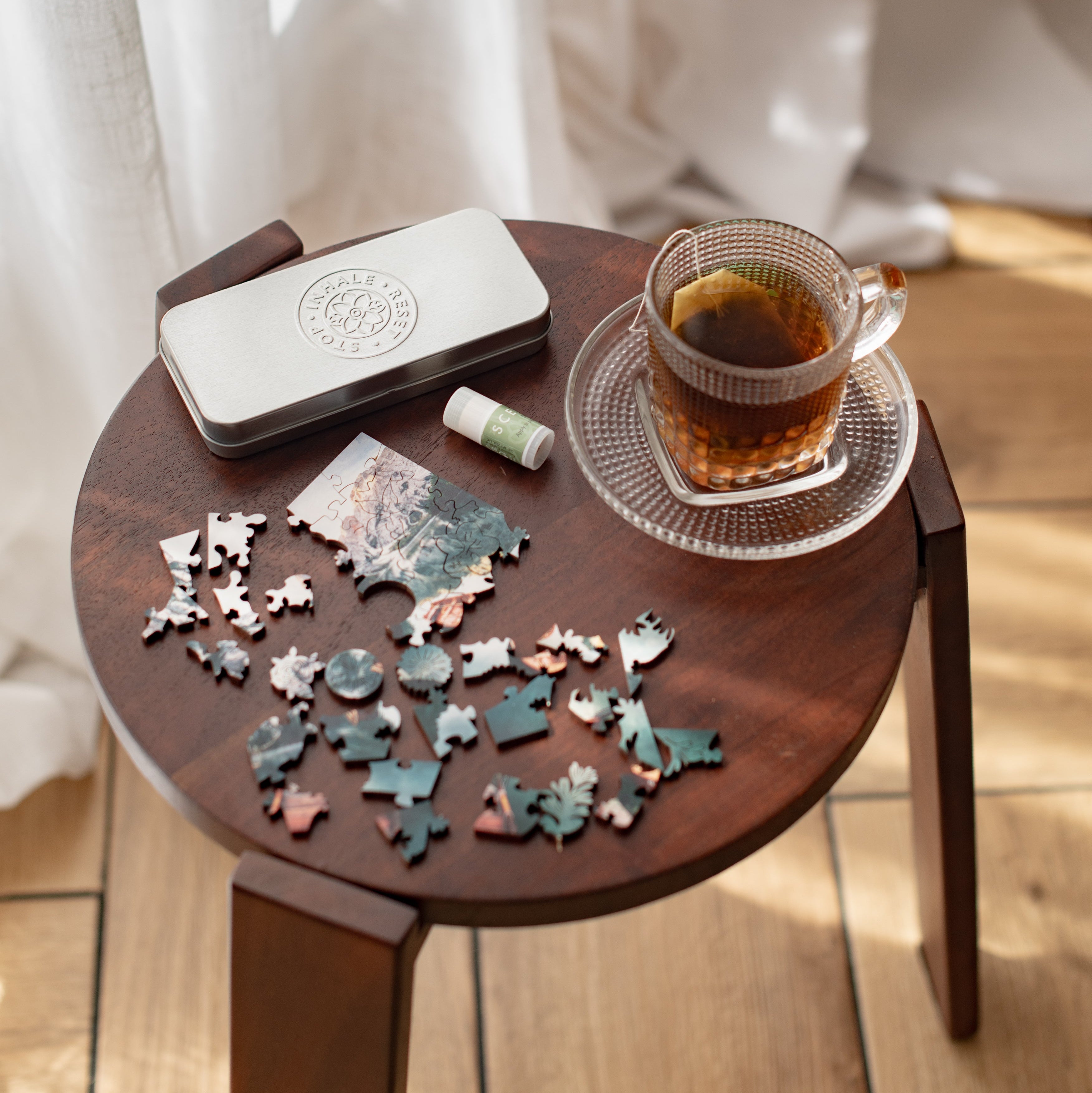 Small wooden table with a puzzle, a tea cup and a change of pace balm set on a light wood floor.