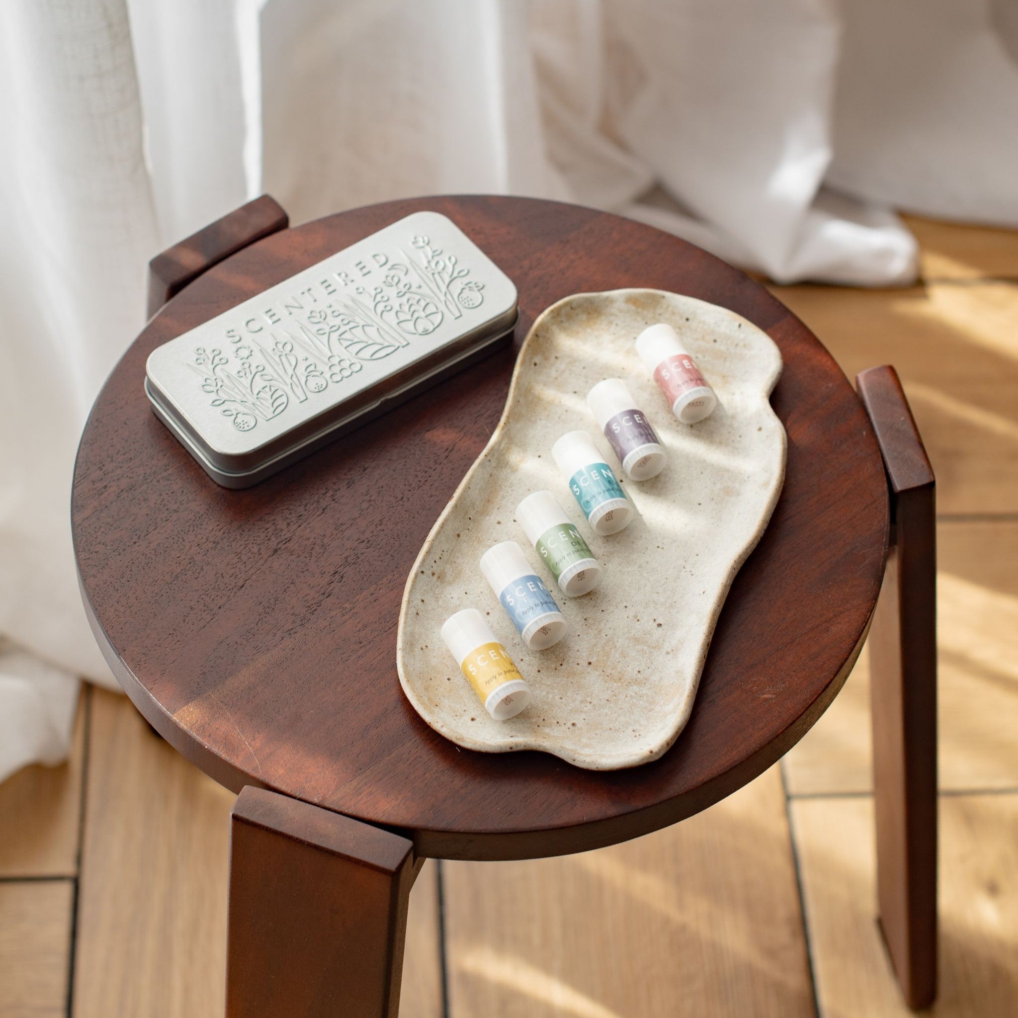 Small wooden table with a ceramic tray holding a set of mini balms and a tin box .