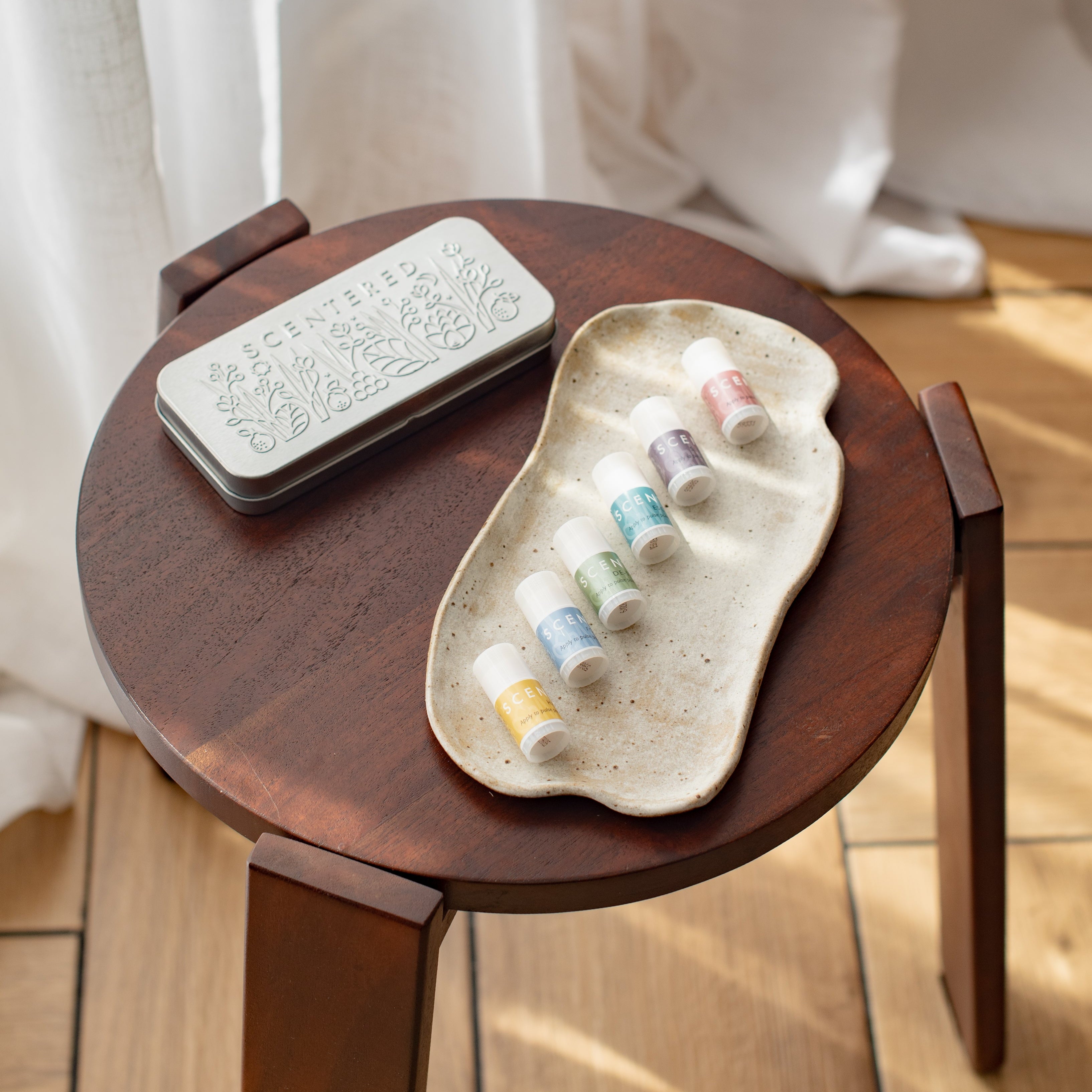 A silver tin, six mini balms, and a plate are placed on the small wooden table.