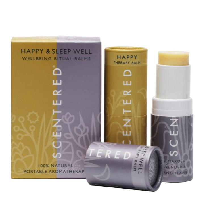 This image showcases Scentered's Wellbeing Ritual Balms for happiness and sleep well. The set includes a "HAPPY THERAPY BALM" and a "SLEEP WELL THERAPY BALM" with ingredients like palmarosa, lavender, and ylang ylang, all presented in 100% natural, portable aromatherapy packaging.