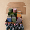 A centered gift box filled with scented candles, a set of gift tins and some balms in stockings.