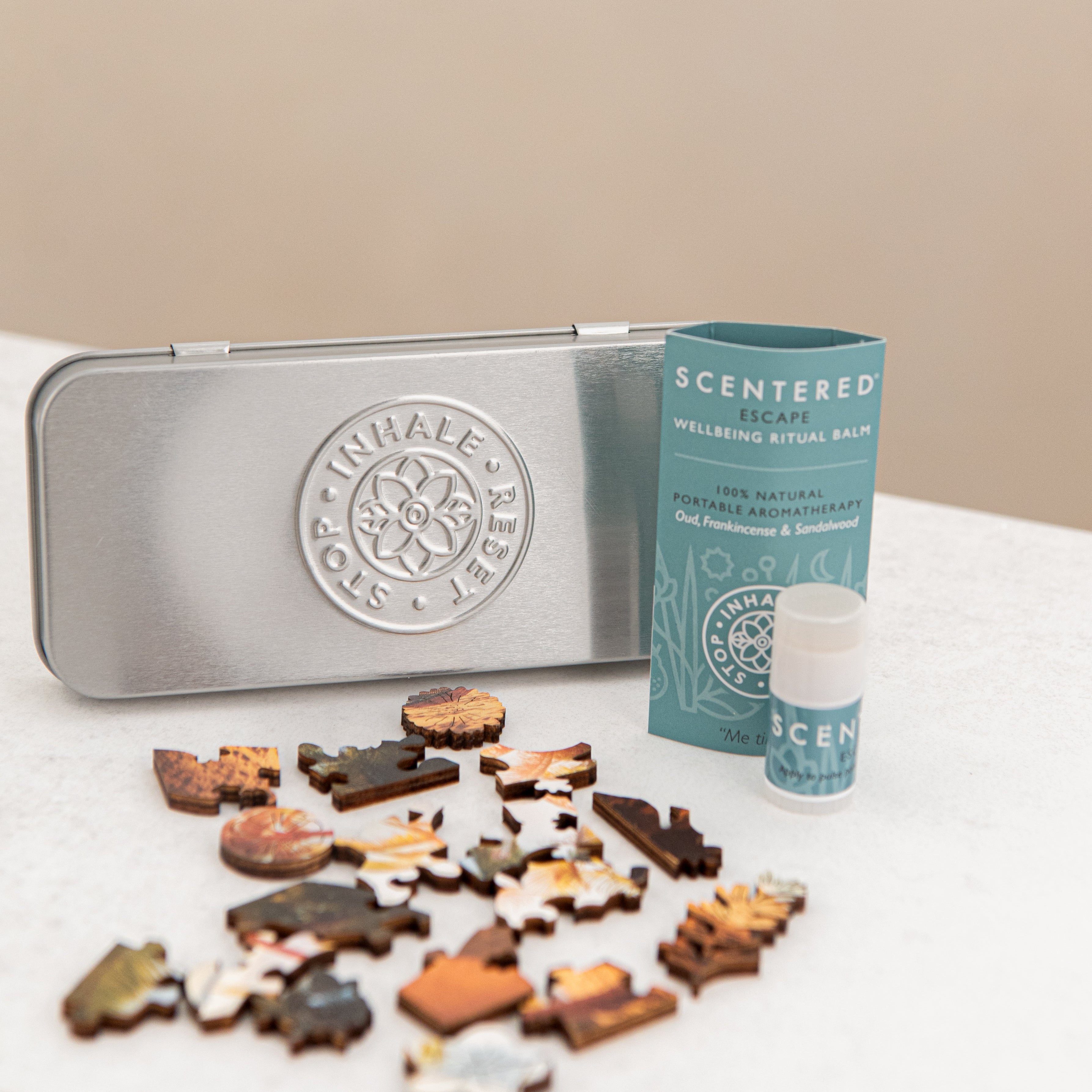Silver tin with Scentered logo, an escape balm and puzzle pieces on a white surface.