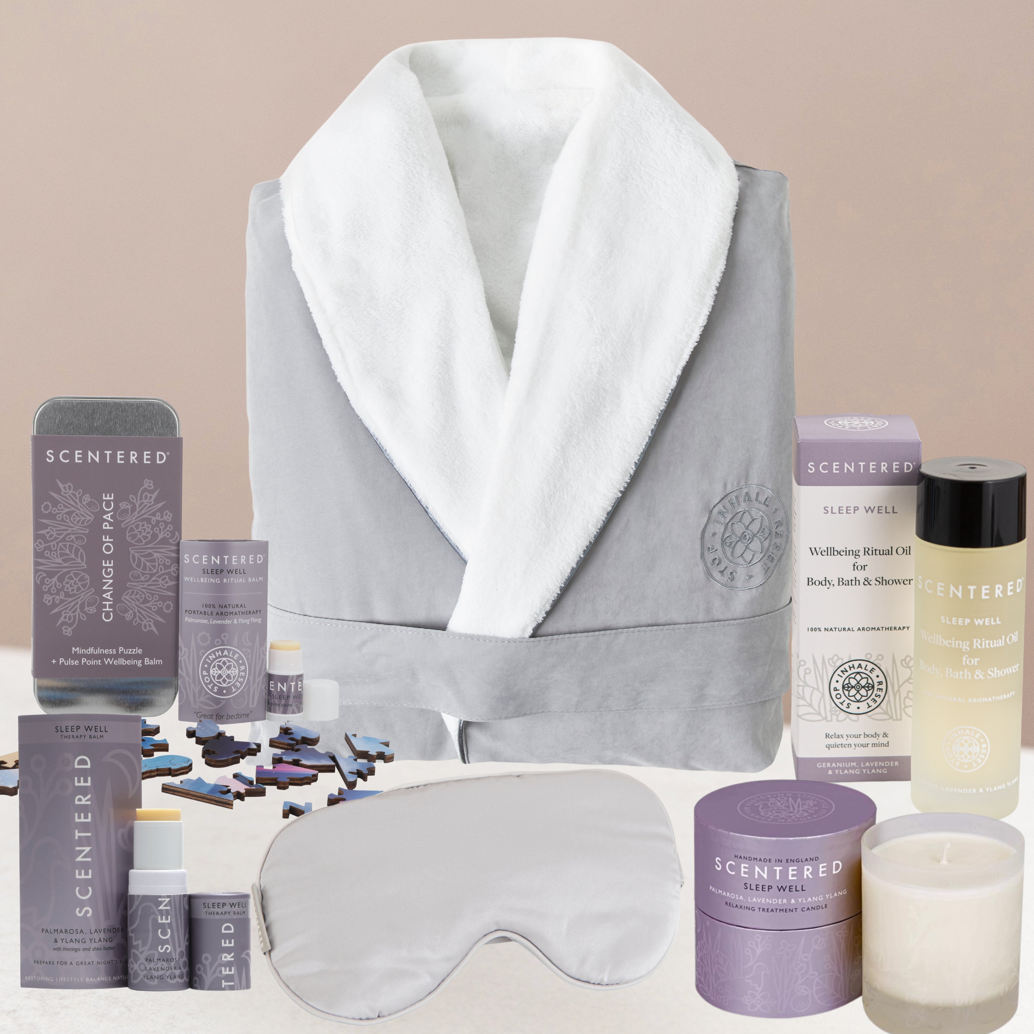 Gray bathrobe with white hood, sleep mask, sleep balm, body oil, candle and various skincare products on a beige background