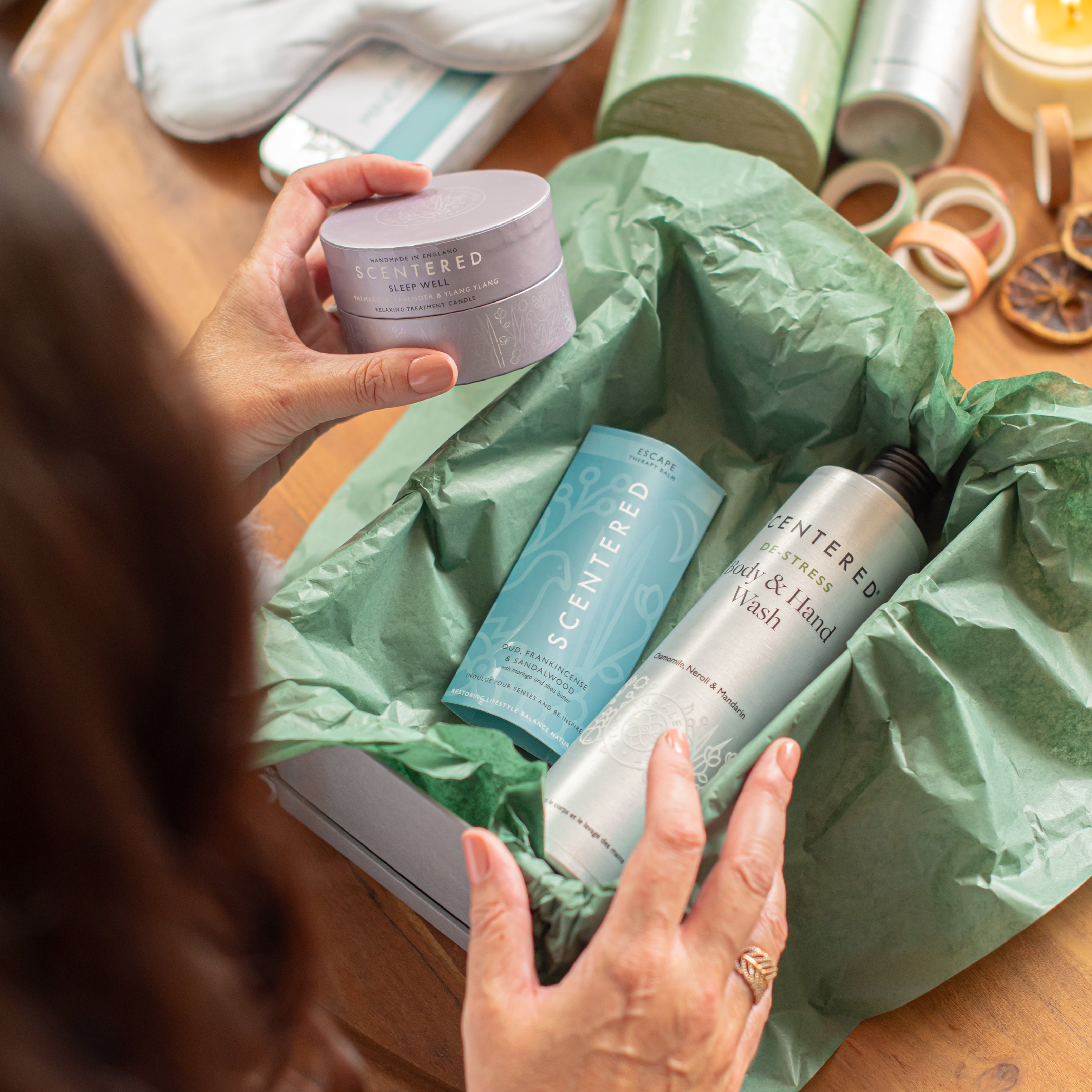 A Woman Touches the Sleep Well Candle from a Gift Box Complete with Escape Balm and HandWash