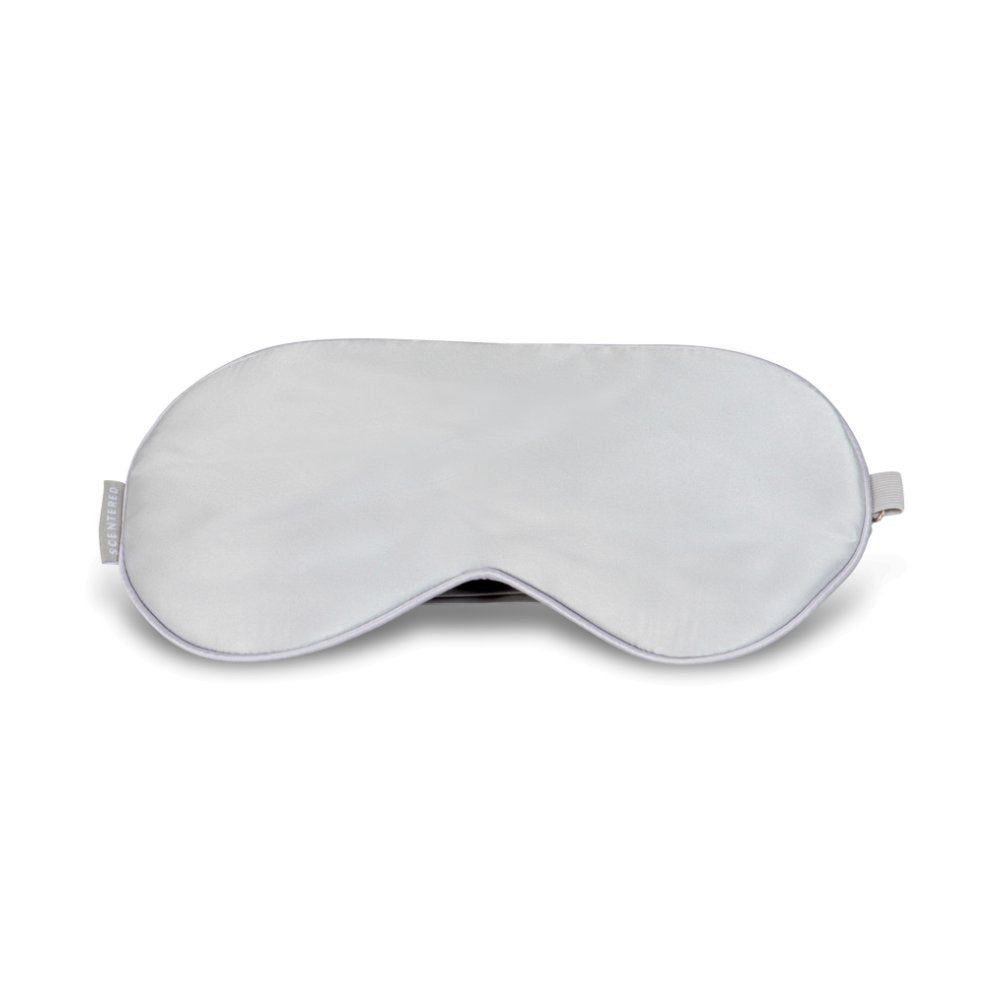 A white silk eye mask with an adjustable strap, designed to cover the eyes and provide light blockage for sleep.