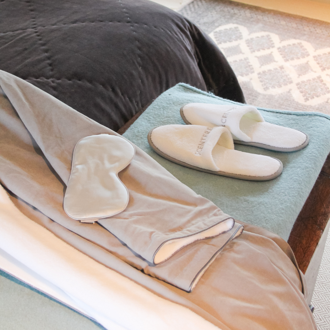 Soft grey sleepwear set with matching eye mask and white Scentered slippers neatly arranged on a bed with a folded blanket, creating a calm and relaxing bedtime atmosphere.