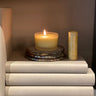 Scentered Be Happy candle burning beside a therapy balm stick on a stack of decorative books, creating a warm and uplifting atmosphere.